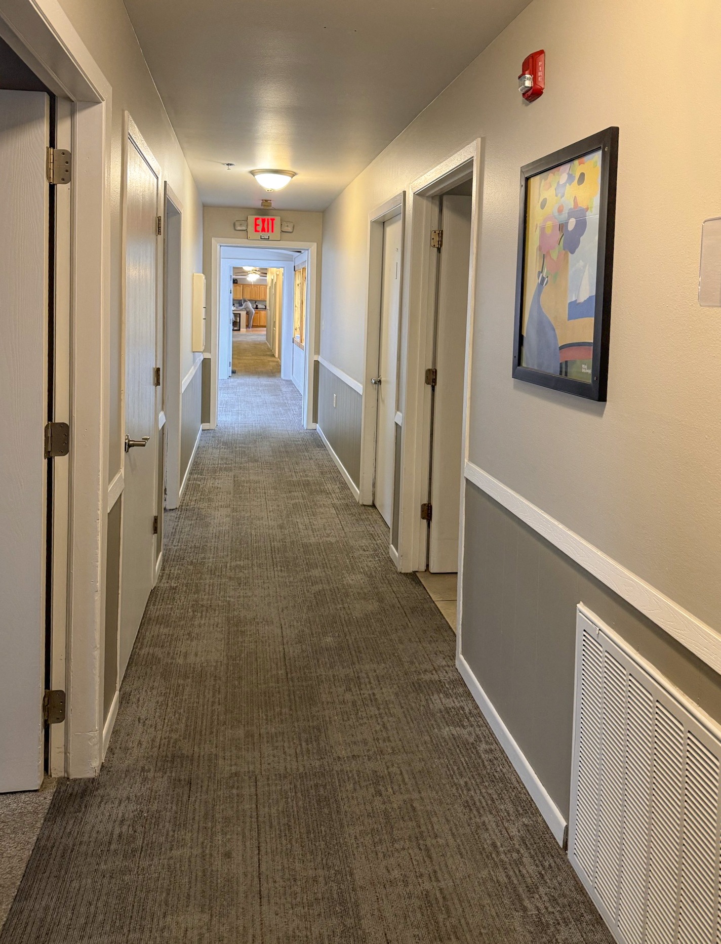 A hallway with a red fire alarm on the wall.